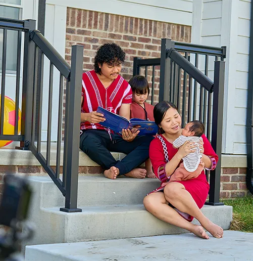 A mom and dad radiate joy on their porch, reading with their young child and holding their baby, celebrating the heartwarming start in their first Habitat for Humanity home.