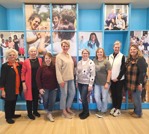 Group of women standing in front of bookshelf in an office space.